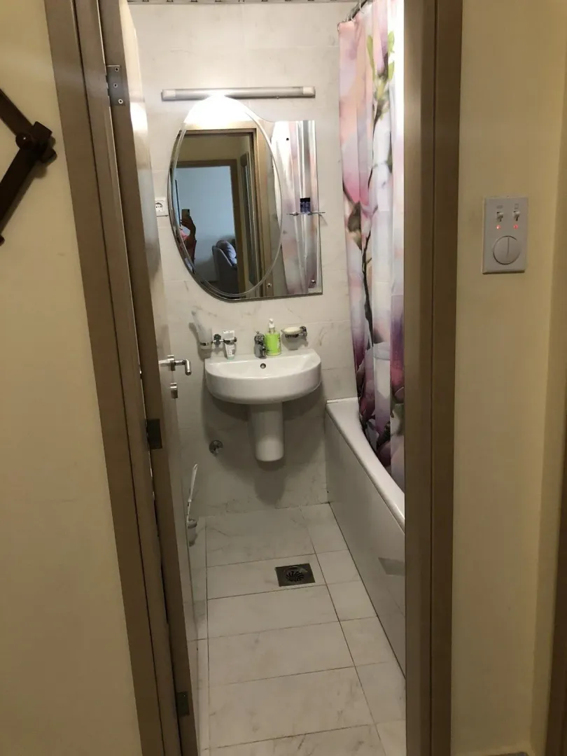 A small bathroom with a white bathtub, sink, and mirror viewed through a doorway.