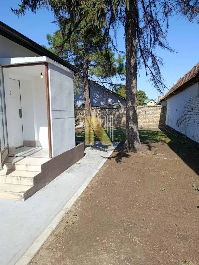 Pogled na dvorište i ulaz u kuću sa stablima i popločanim stazama.