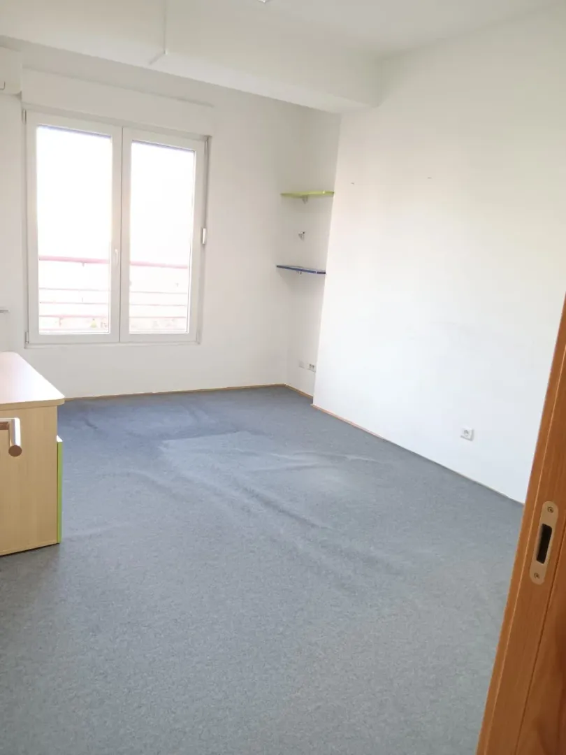 Empty room with a window and a grey carpet.