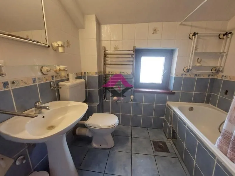 Kupatilo sa plavim i belim pločicama, umivaonikom, wc šoljom i kadom.