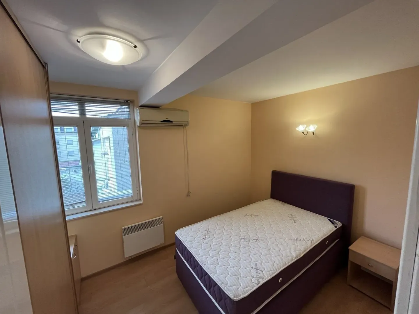 Svijetla spavaća soba sa bračnim krevetom, ormarom i klima uređajem.
