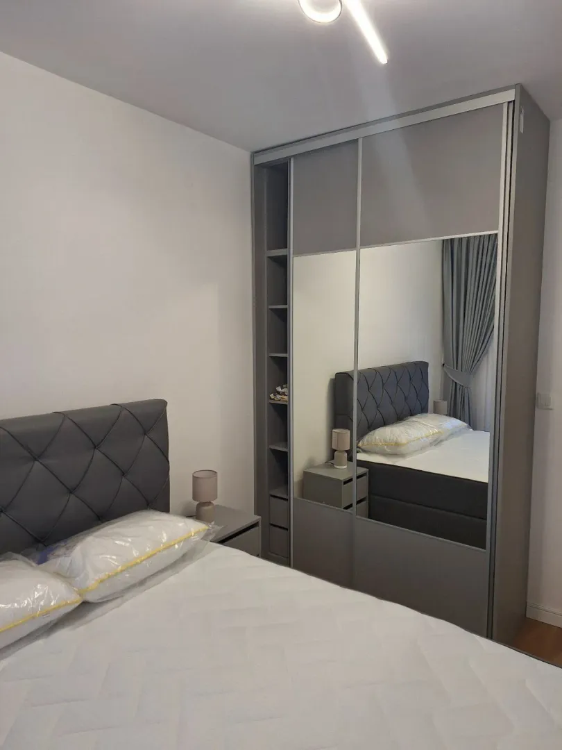 Svijetla spavaća soba sa modernim sivim krevetom i velikim ugradnim plakarem sa ogledalima.