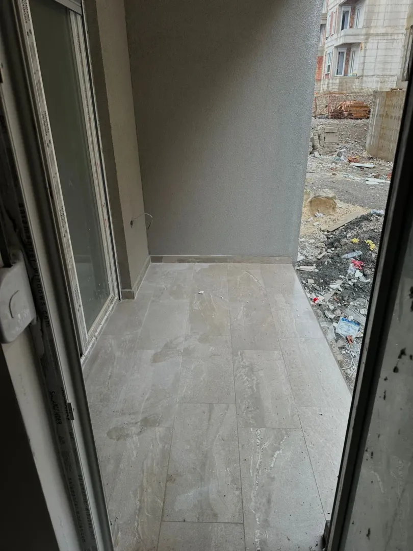 Nenamješten balkon sa popločanim podom i pogledom na gradilište.