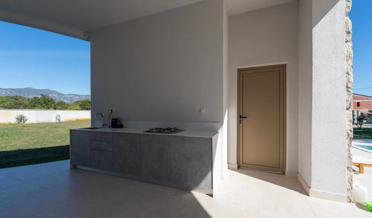 Covered terrace with an outdoor kitchen and a door leading inside.