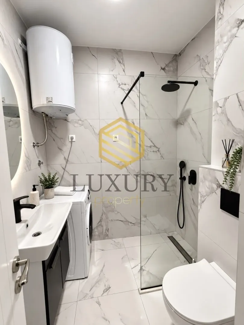 Modernly equipped bathroom with a walk-in shower, washbasin, and washing machine.