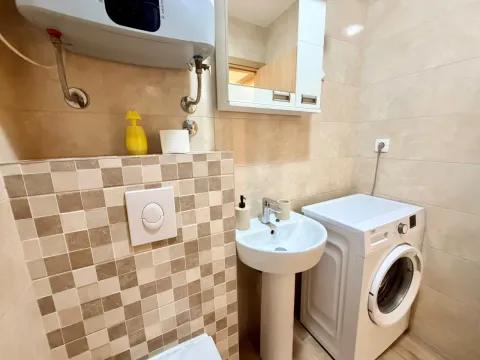 Manje kupatilo sa umivaonikom, veš mašinom, bojlerom i pločicama u bež tonovima. - image 13