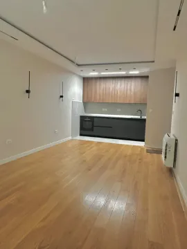 Living room with wooden flooring and a built-in kitchen in the background. - image 4