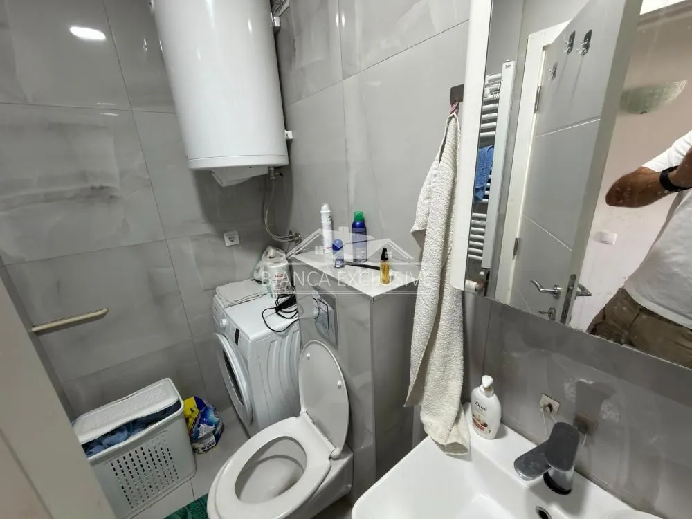 Manje kupatilo opremljeno sanitarijama, tuš kabinom, umivaonikom i veš mašinom.