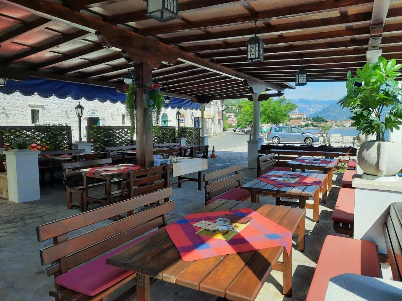 Natkrivena terasa restorana sa drvenim stolovima i klupama.