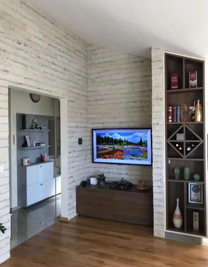 Living room with a decorative stone wall, television, and built-in shelving unit.