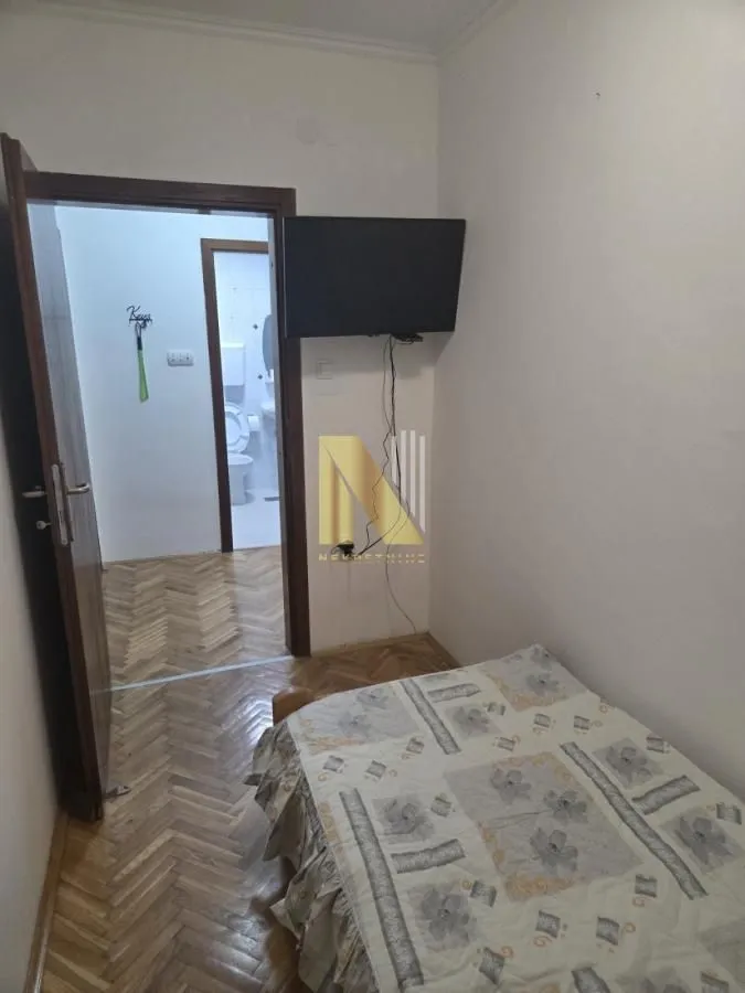 Manja spavaća soba sa krevetom i televizorom na zidu.