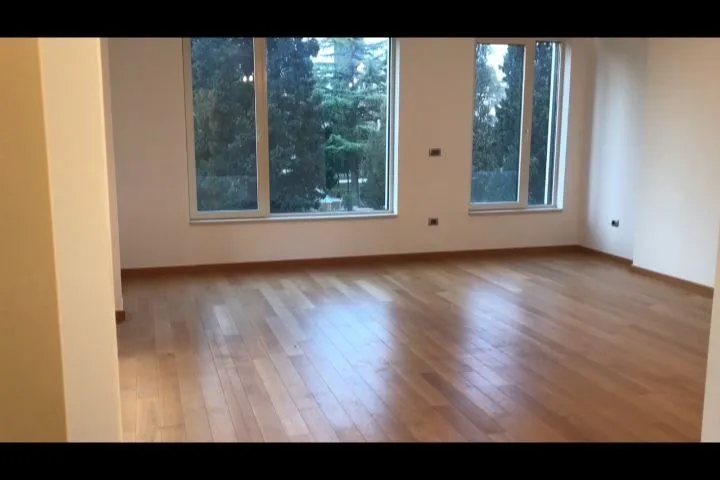 Prazna i prostrana soba sa drvenim podom i velikim prozorima.