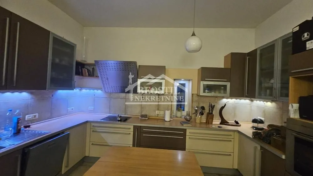 Opremljena kuhinja u obliku slova U sa elementima u braon tonovima i radnom površinom.