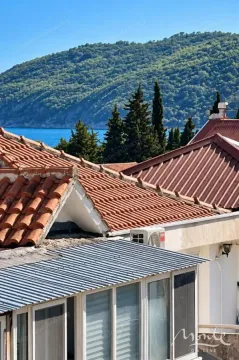 Pogled na krovove kuća, zelenilo i more u daljini. - image 2
