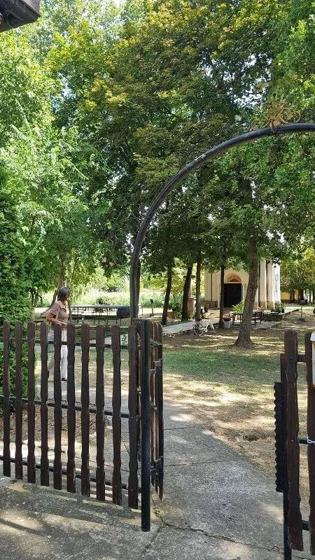 Pogled kroz drvenu kapiju na dvorište i zelenilo ispred kuće.