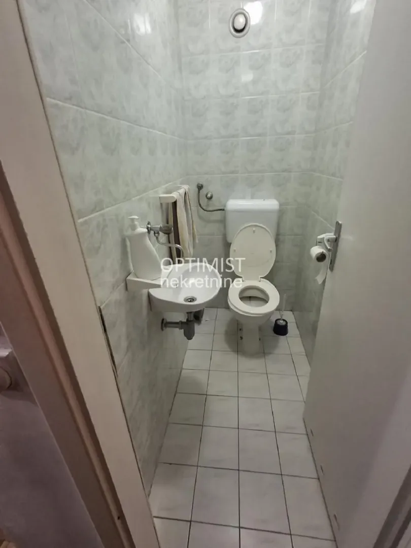 Manje kupatilo sa toaletom i umivaonikom, obloženo keramičkim pločicama.