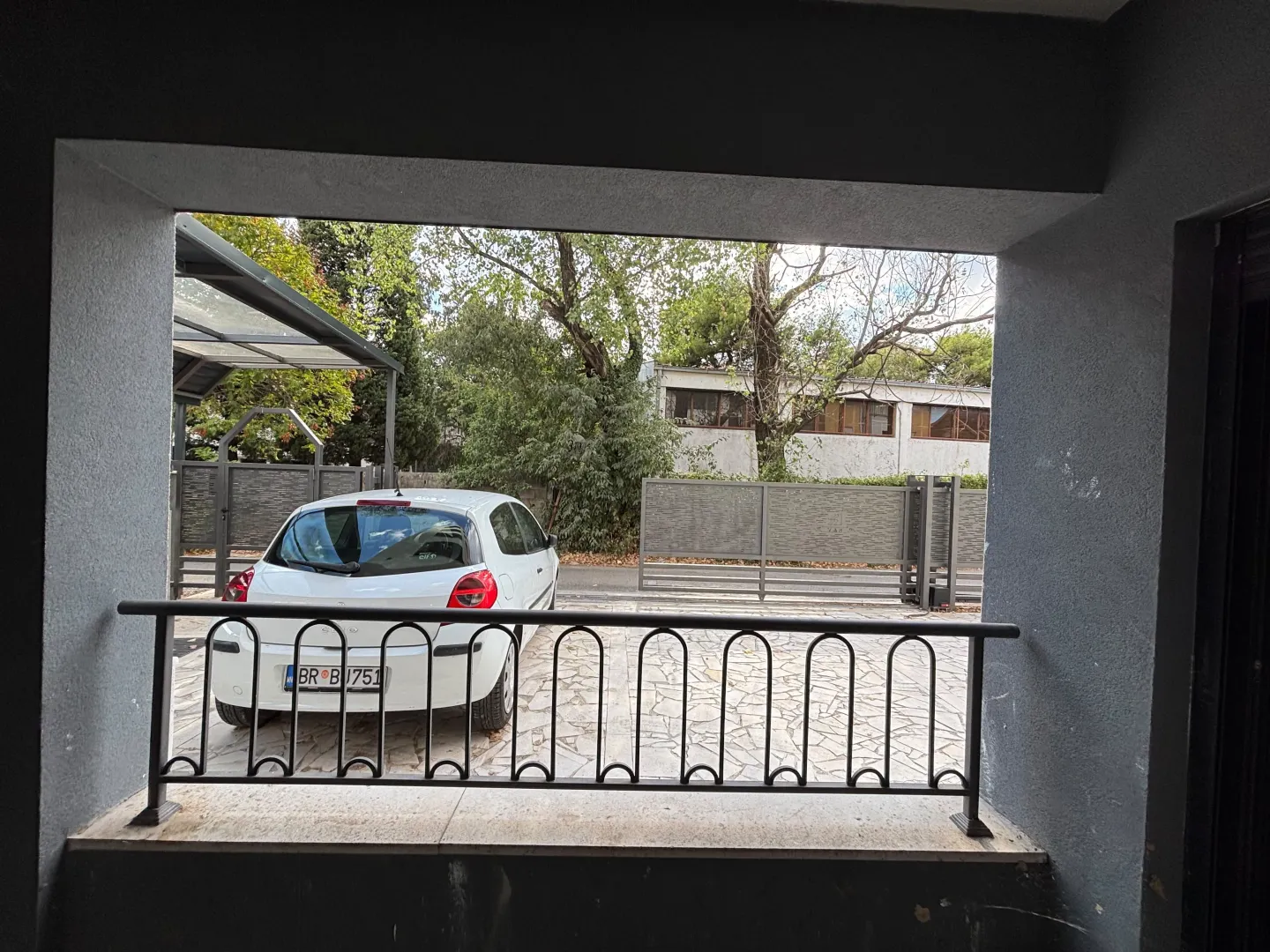 Pogled iz dvorišta na parking prostor ispred kuće sa parkiranim automobilom.