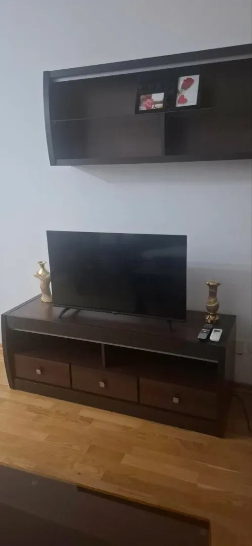 Dnevna soba sa TV komodom i policom na zidu.