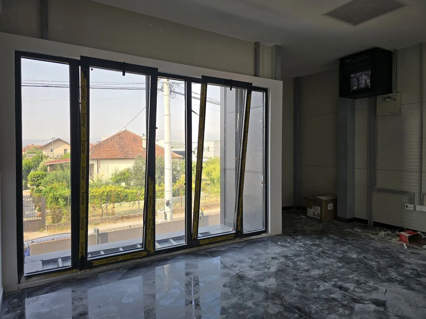 A view of an unfinished room under construction with large windows and tiled flooring.