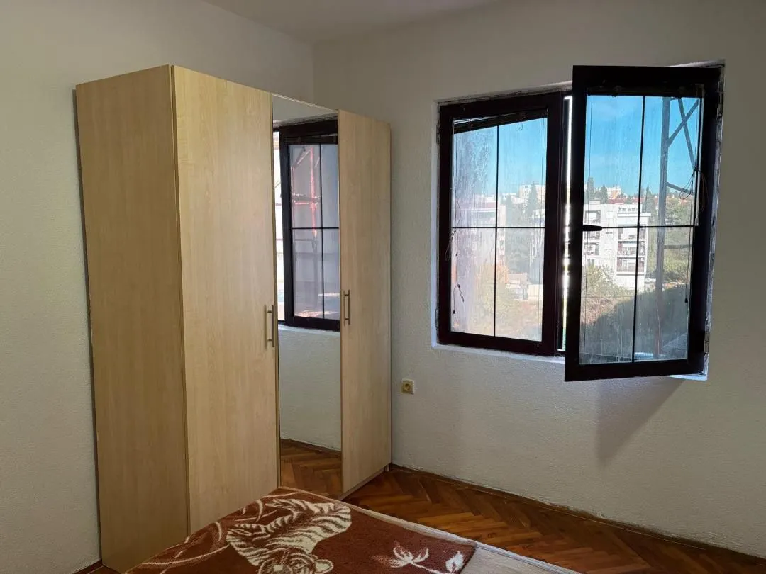 Manja spavaća soba sa ormarom i prozorom koji gleda na grad.