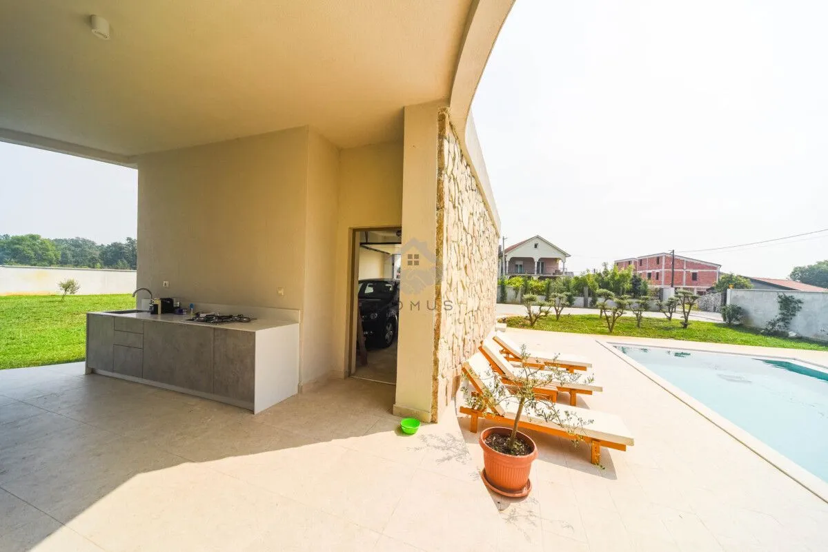 Covered terrace with an outdoor kitchen and a view of the pool and yard.