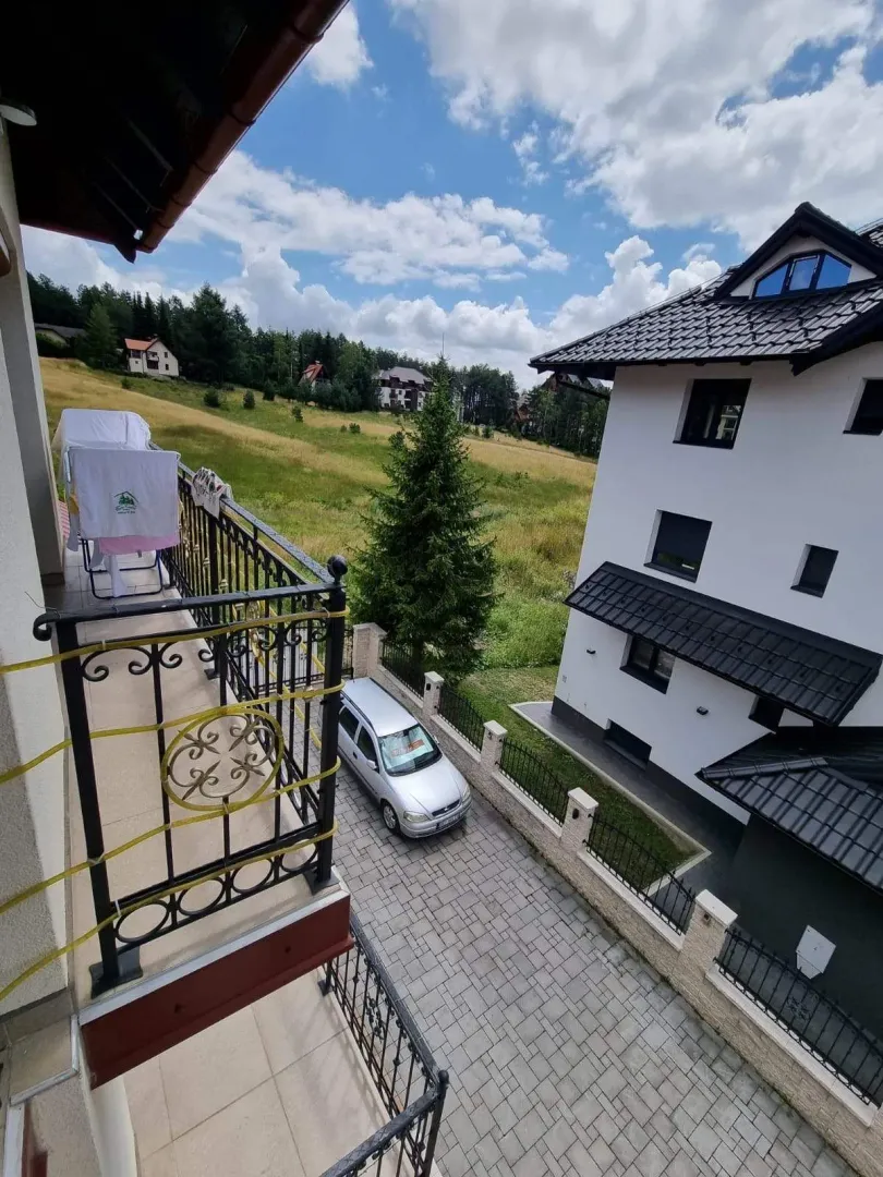 Pogled sa balkona na dvorište, susednu kuću i prirodu.