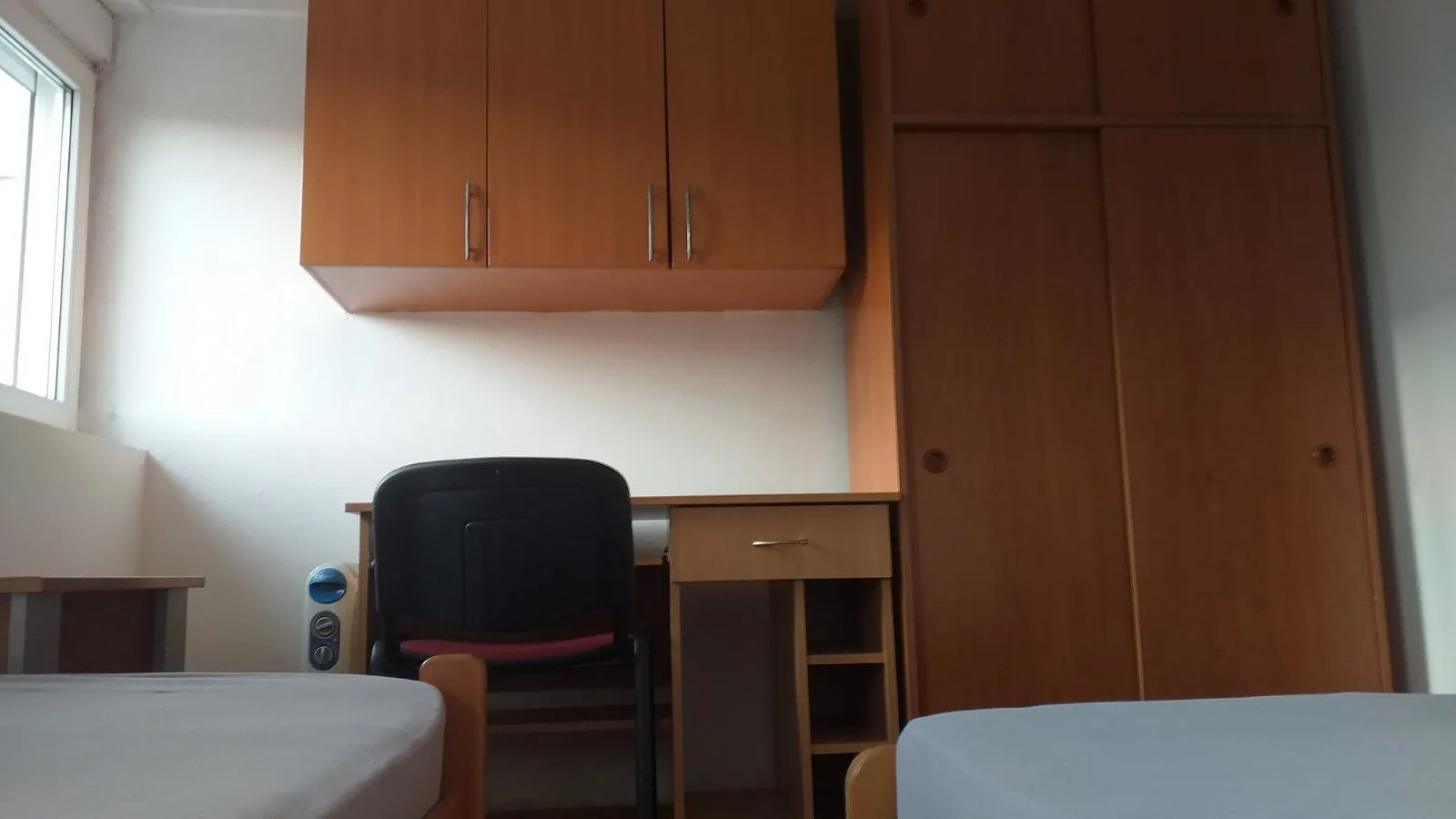 A room with a desk, wardrobe, and beds.