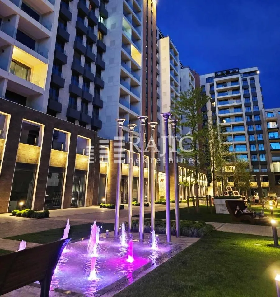 Evening view of the courtyard and residential building facade with a fountain.