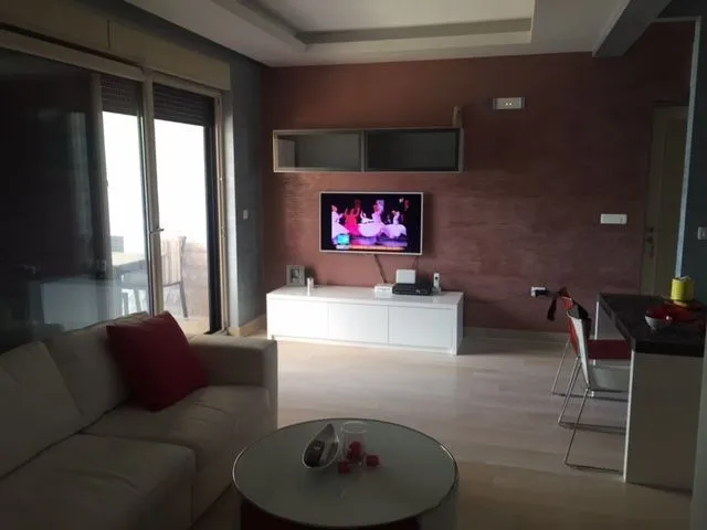 Dnevna soba sa sofom, klub stolom i televizorom montiranim na zid.