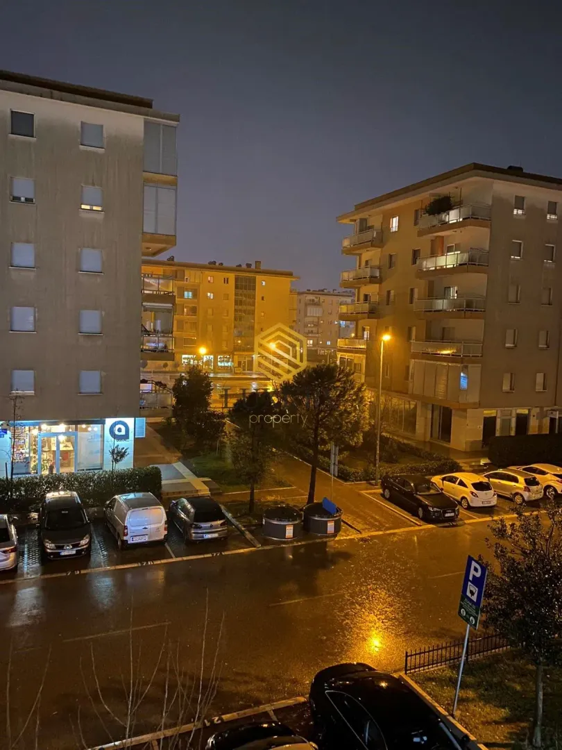 Noćni pogled sa terase na zgrade i osvetljeni parking.