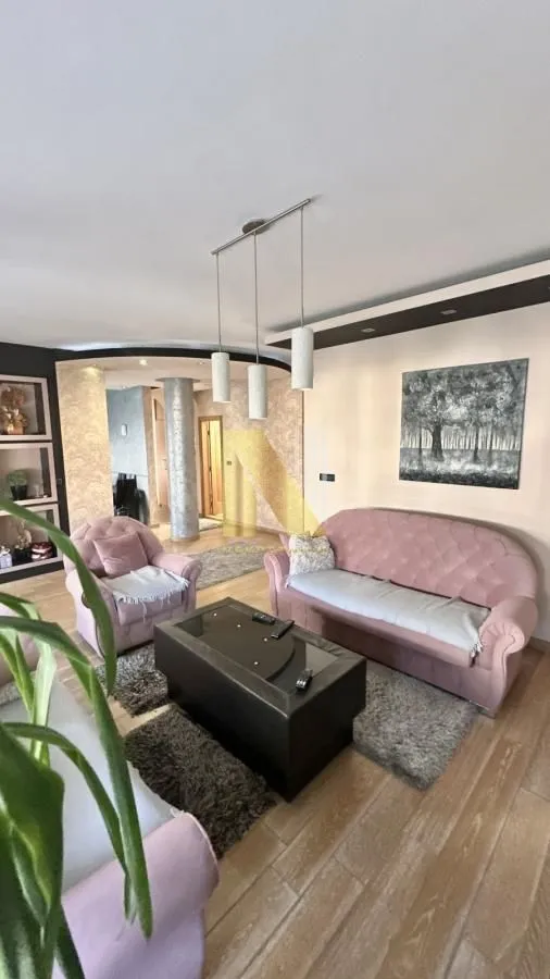 Dnevna soba sa roze garniturom i trpezarijom u pozadini.