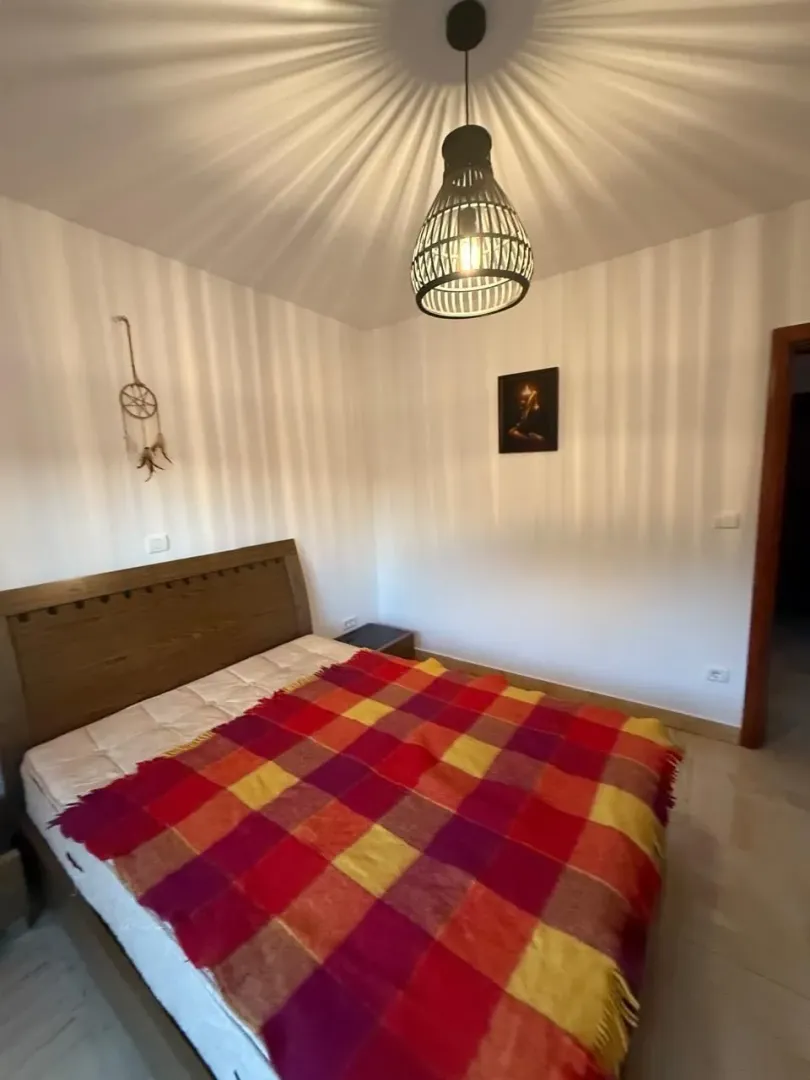 Spavaća soba sa bračnim krevetom, šarenim prekrivačem i lusterom na plafonu.