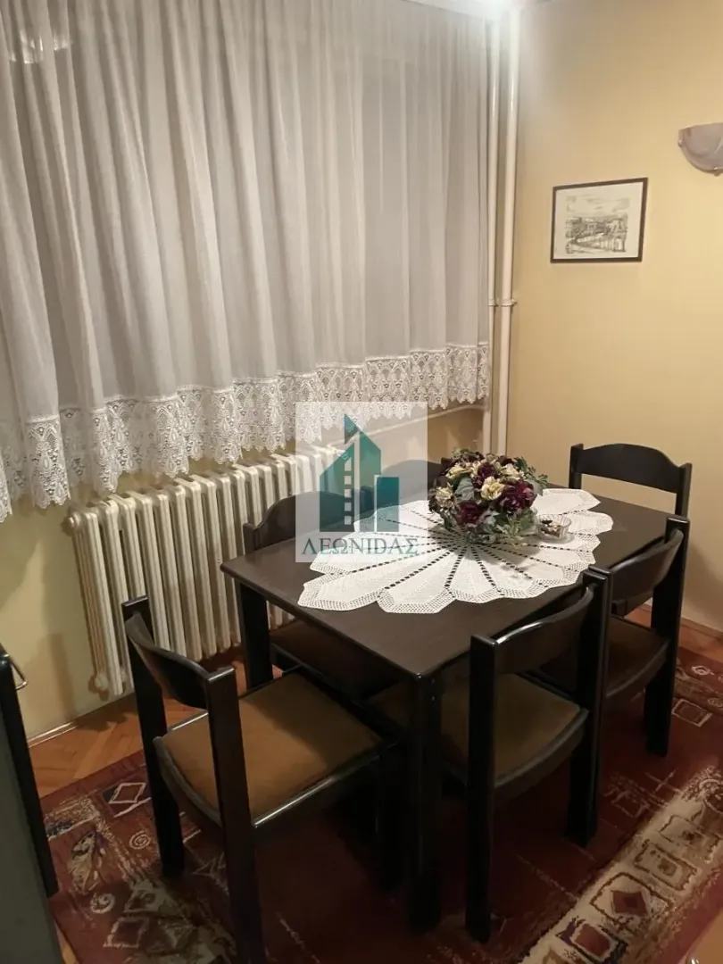 Dining table with chairs placed next to a window with white curtains.