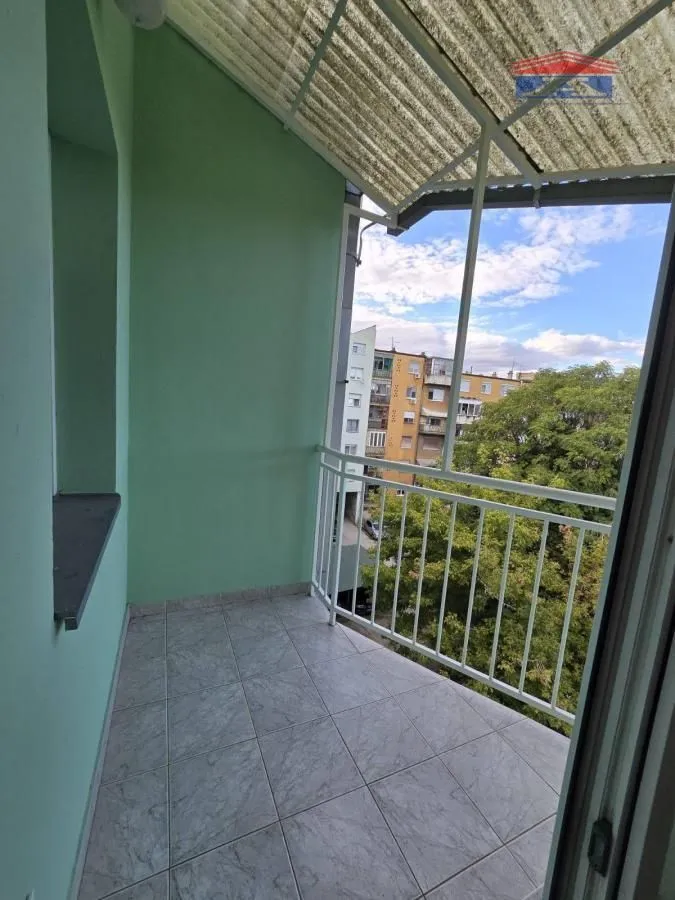 Natkriveni balkon sa popločanim podom i pogledom na okolne zgrade i zelenilo.