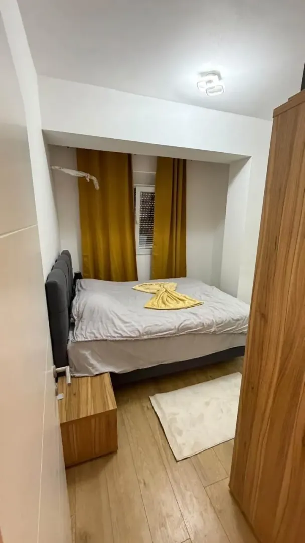 Manja spavaća soba sa bračnim krevetom, žutim zavesama i ormarom.
