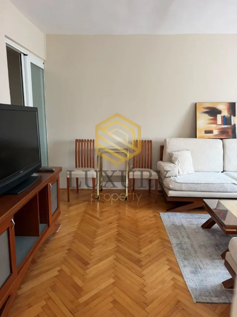 Living room with sofa, TV and parquet flooring.