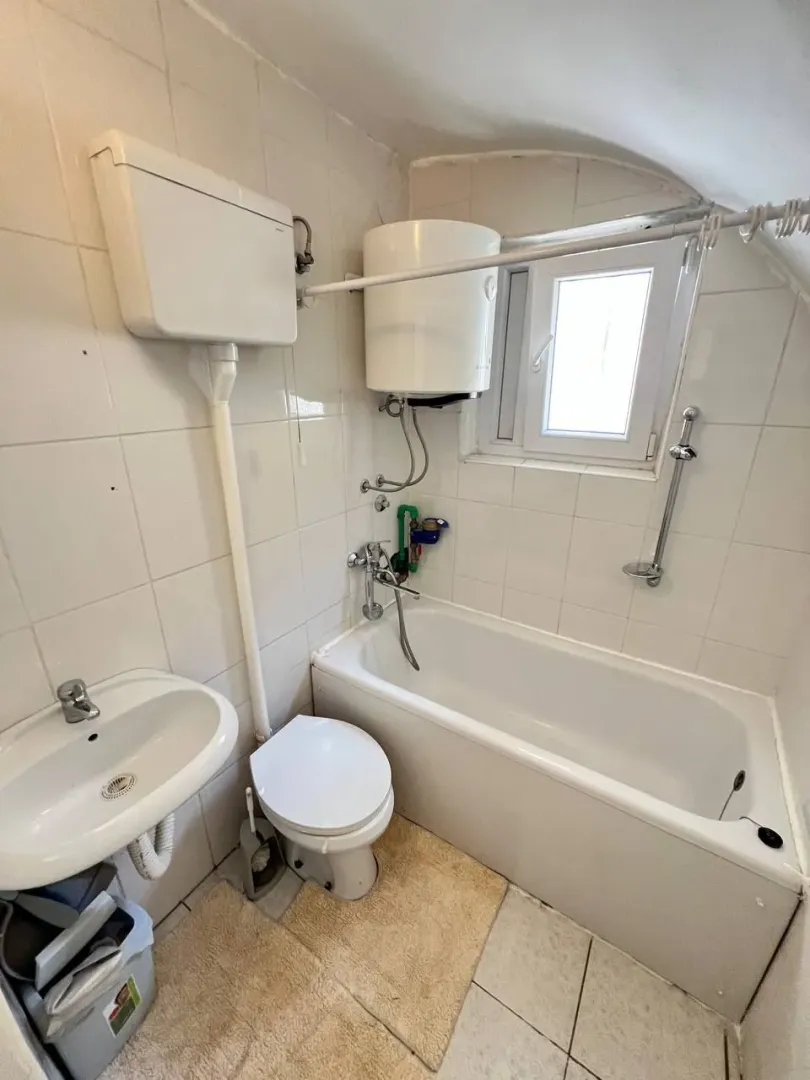 Manje kupatilo sa kadom, umivaonikom i wc šoljom obloženo bijelim pločicama.