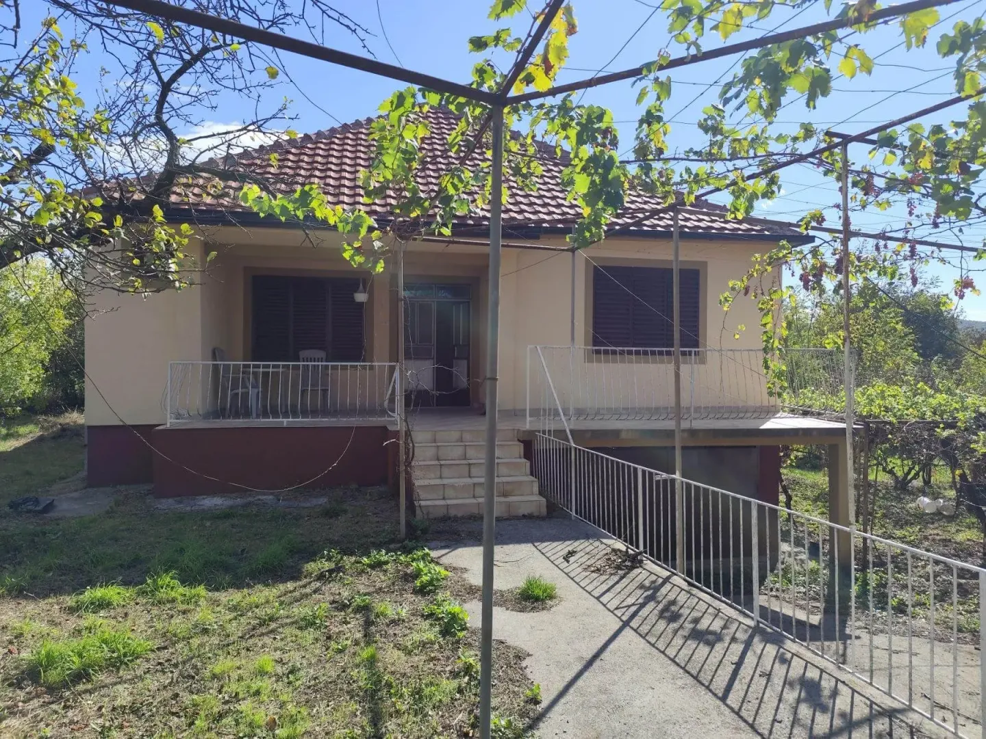 Prednji dio kuće sa terasom, dvorištem i pergolom sa vinovom lozom.