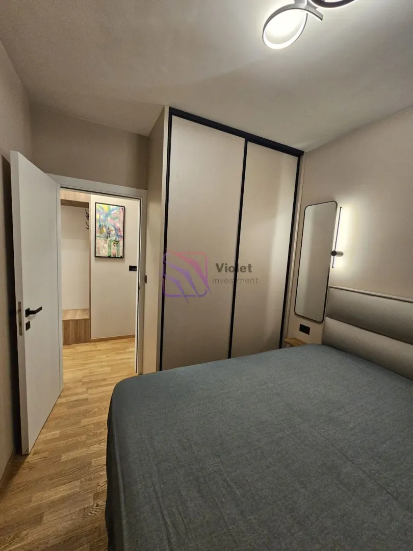 Furnished bedroom with a double bed, wardrobe, and an entrance hallway visible in the background.