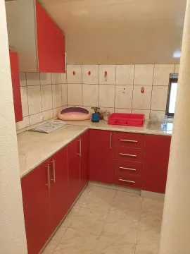 Mala kuhinja sa crvenim elementima i svijetlom radnom površinom. - image 7