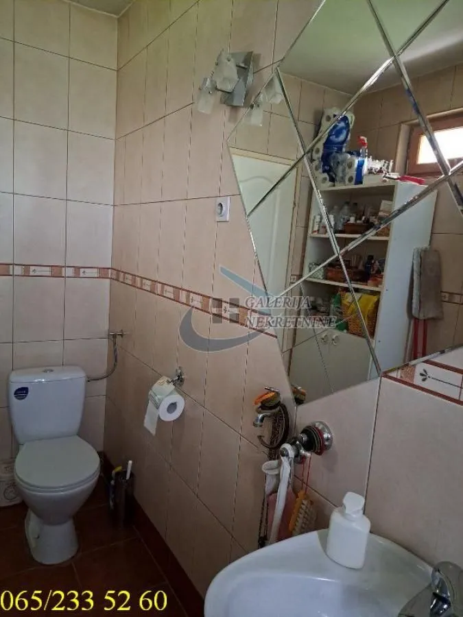 Manje kupatilo obloženo keramičkim pločicama sa toaletom, umivaonikom i velikim ogledalom.