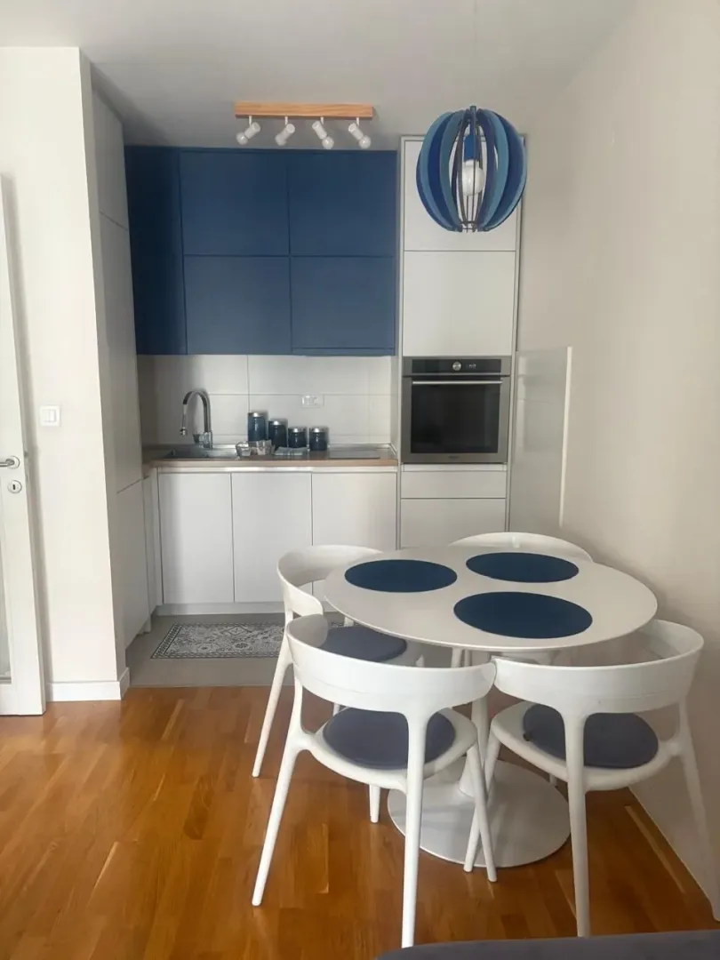 Small kitchen with a dining table and white chairs.