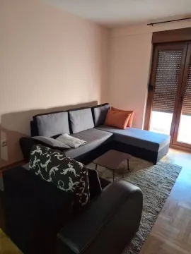 Living room with a sectional sofa, coffee table, and balcony doors. - image 2