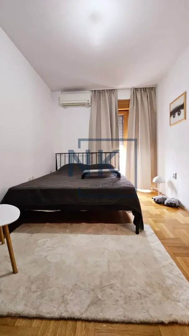 Furnished bedroom with a double bed, air conditioning, and a window with curtains.