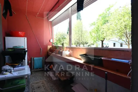 Natkriveni balkon sa crvenim zidom i pogledom na zelenilo. - image 12