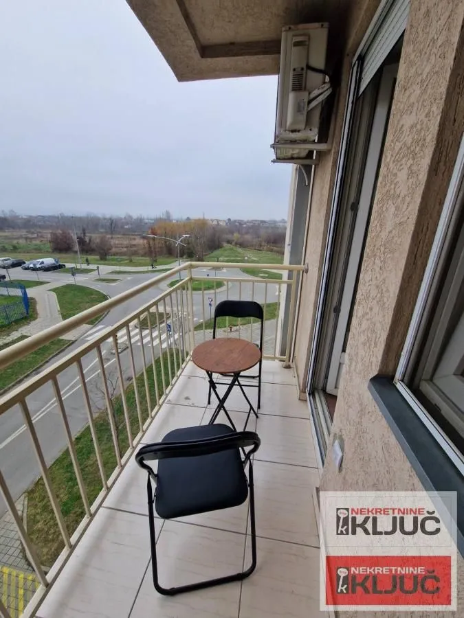 Nameštena terasa sa malim stolom i stolicama i pogledom na ulicu.