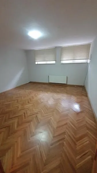 Prazna soba sa drvenim parketom i dva prozora.