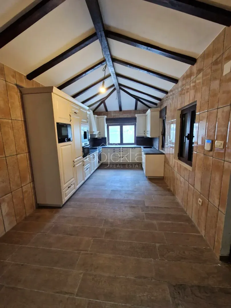 Kitchen with white cabinetry, tiled walls, and exposed wooden ceiling beams.