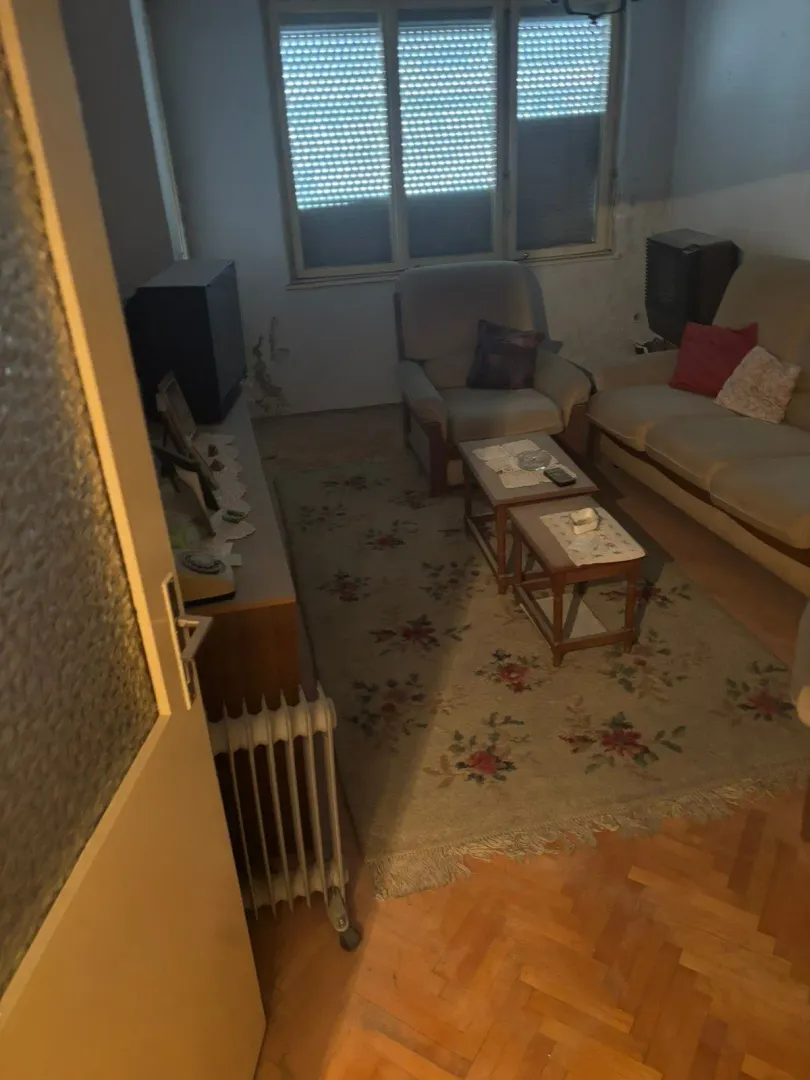 Dnevna soba sa garniturom, stočićem i prozorom sa roletnama.