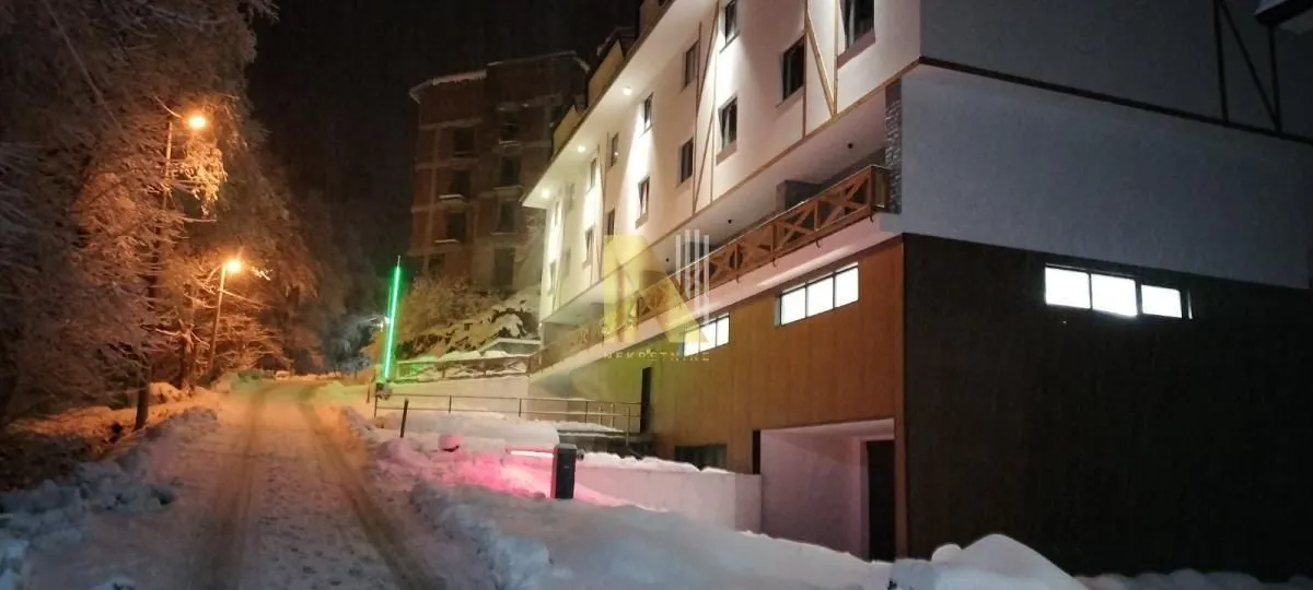 Noćni prikaz eksterijera zgrade okružene snegom.